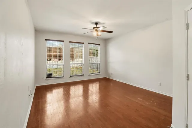 an empty room with wooden floor chandelier fan and windows
