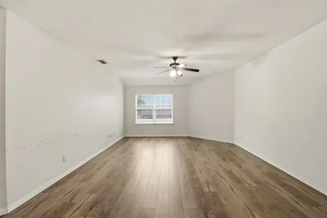 an empty room with wooden floor chandelier fan and windows