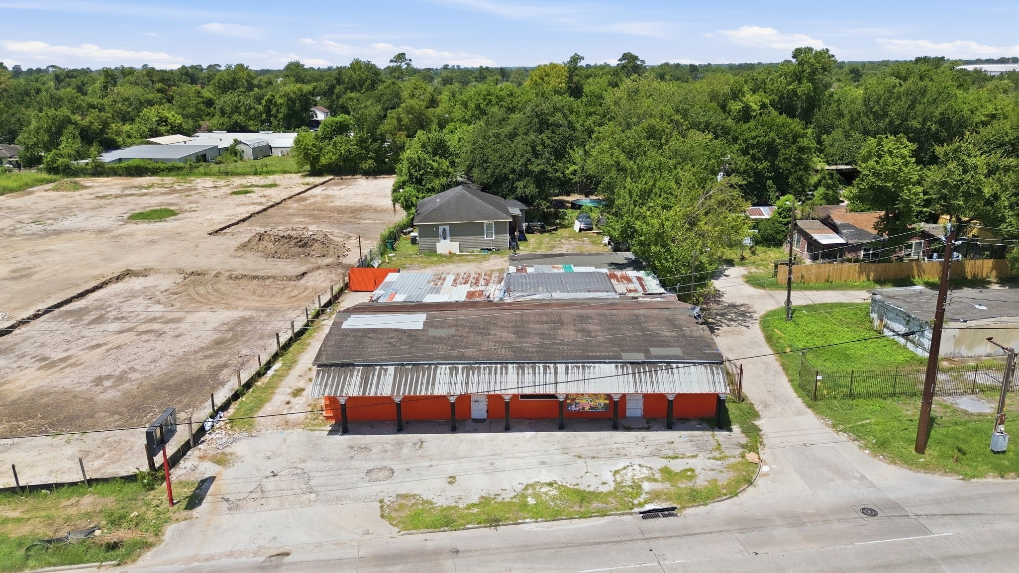 7715 West Hardy Road Houston, TX 77022 - Photo 3 of 19 Expansive lot with a mix of cleared land and mature trees, featuring a central structure with a rustic, industrial facade. Ideal for redevelopment or creative projects, surrounded by lush greenery and a serene setting.