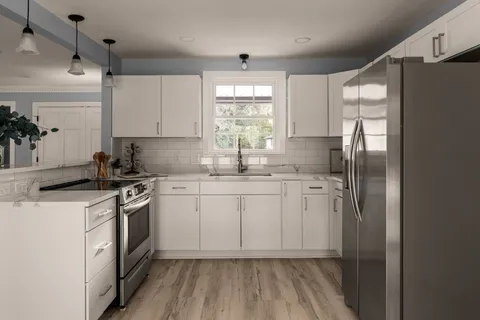 a kitchen with stainless steel appliances granite countertop a refrigerator a sink dishwasher a stove and white countertops with wooden floor