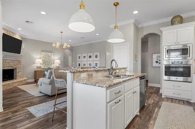 a kitchen with stainless steel appliances kitchen island granite countertop a stove top oven a sink a dining table and chairs with wooden floor