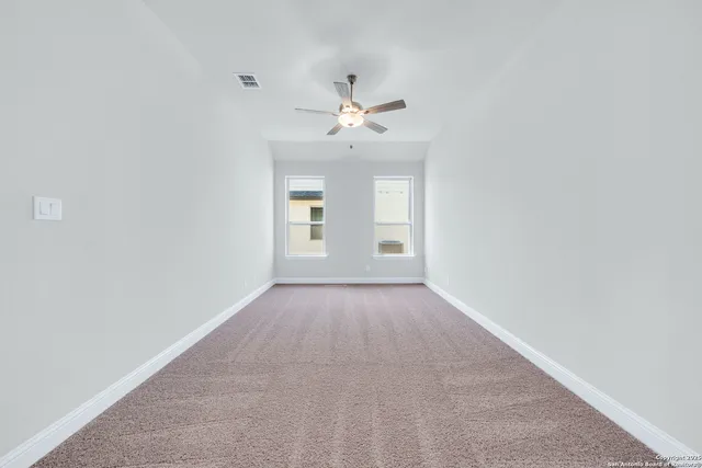 an empty room with chandelier fan and windows