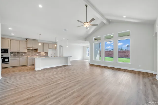 a view of an empty room and kitchen with wooden floor