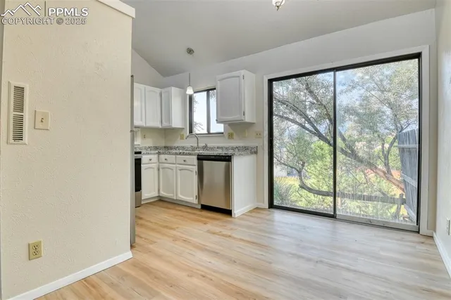 a kitchen with stainless steel appliances granite countertop a stove a sink and white cabinets with wooden floor next to windows