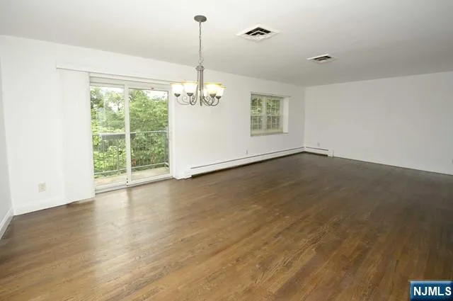 a view of an empty room with wooden floor fridge and a window