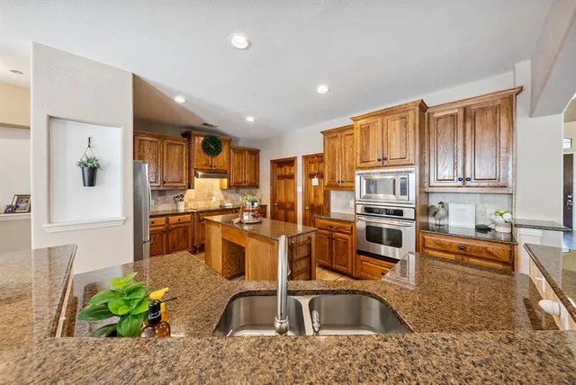 a kitchen with stainless steel appliances granite countertop a refrigerator a stove and a sink with wooden floor