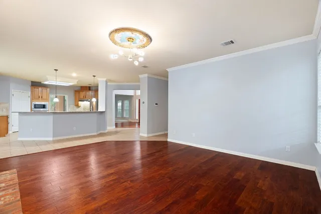 a view of an empty room with wooden floor and a kitchen