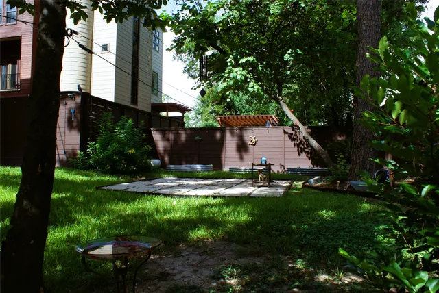 a backyard of a house with plants and large tree