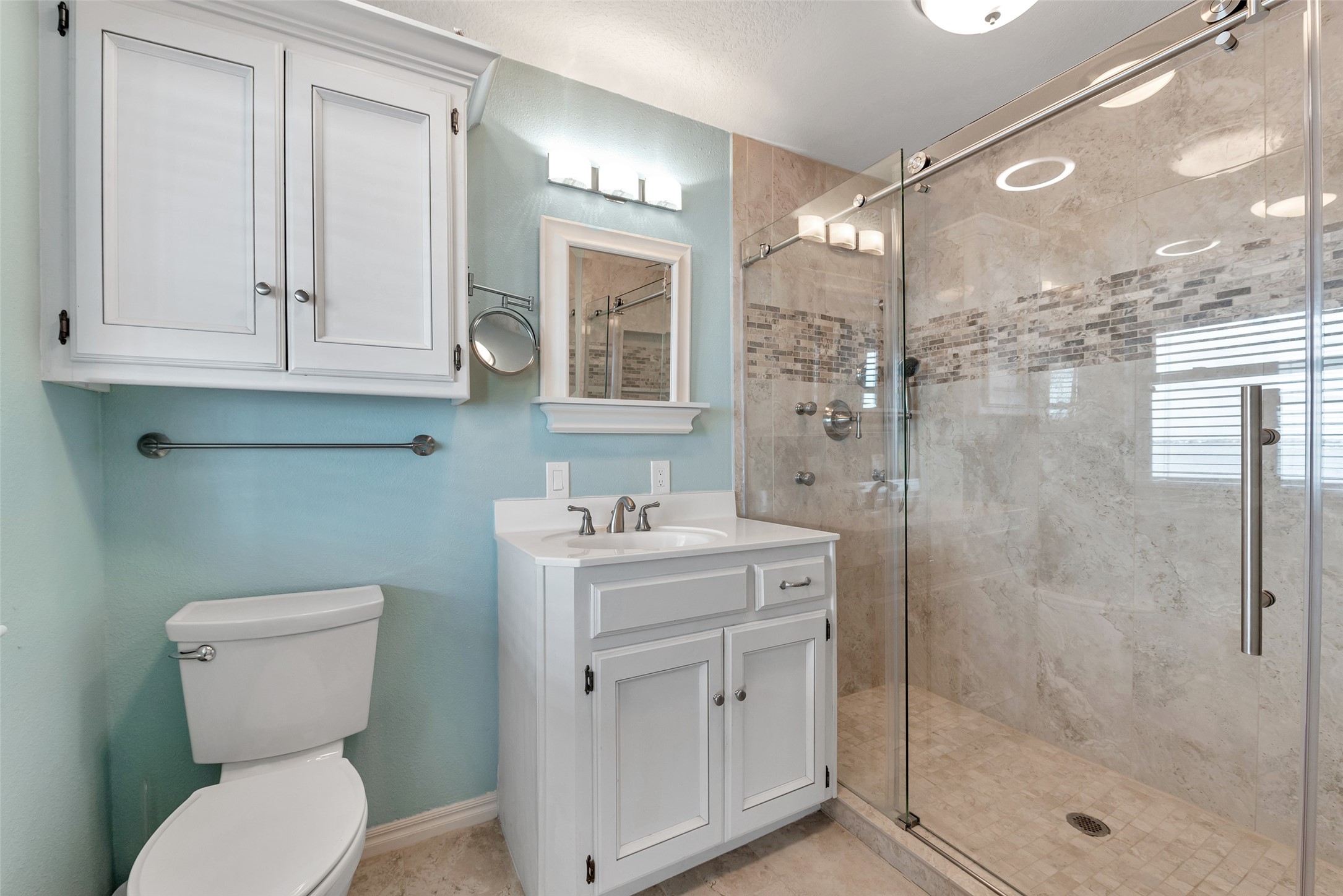 247 Isles End Road Tiki Island, TX 77554 - Photo 25 of 48 Enjoy the spa-like feel of this beautifully updated ensuite featuring a walk-in tile shower with glass enclosure, white vanity, and linen cabinetry for added storage. Clean lines and soft tones create a calming retreat.