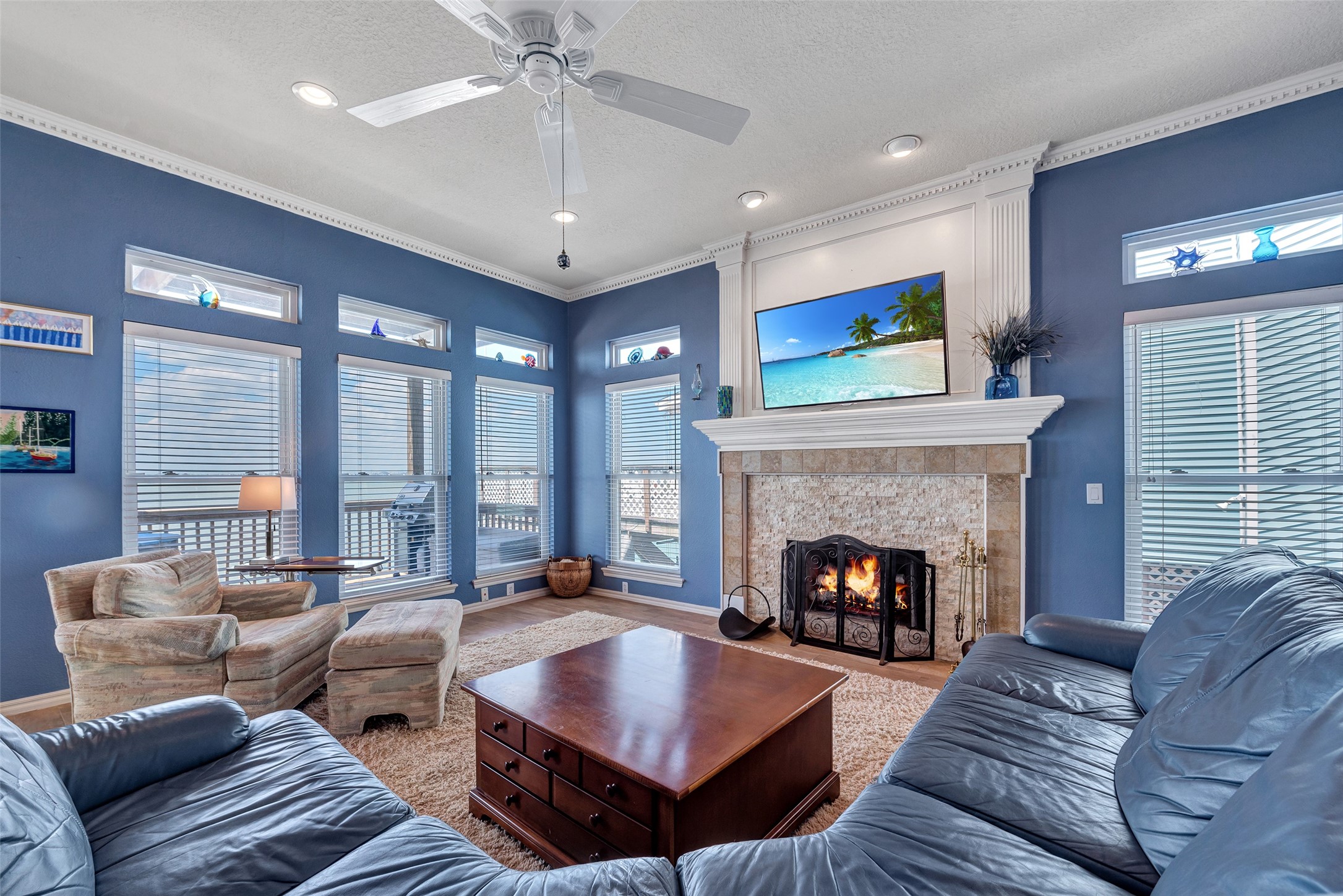 247 Isles End Road Tiki Island, TX 77554 - Photo 5 of 48 Tall ceilings, crown molding, and a wall of bay-facing windows make this living room feel open and inviting. With a wood-burning fireplace and easy deck access, it’s the perfect spot to unwind or gather with friends.