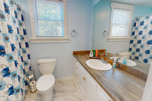 a bathroom with a granite countertop toilet a sink a mirror a window and a shower