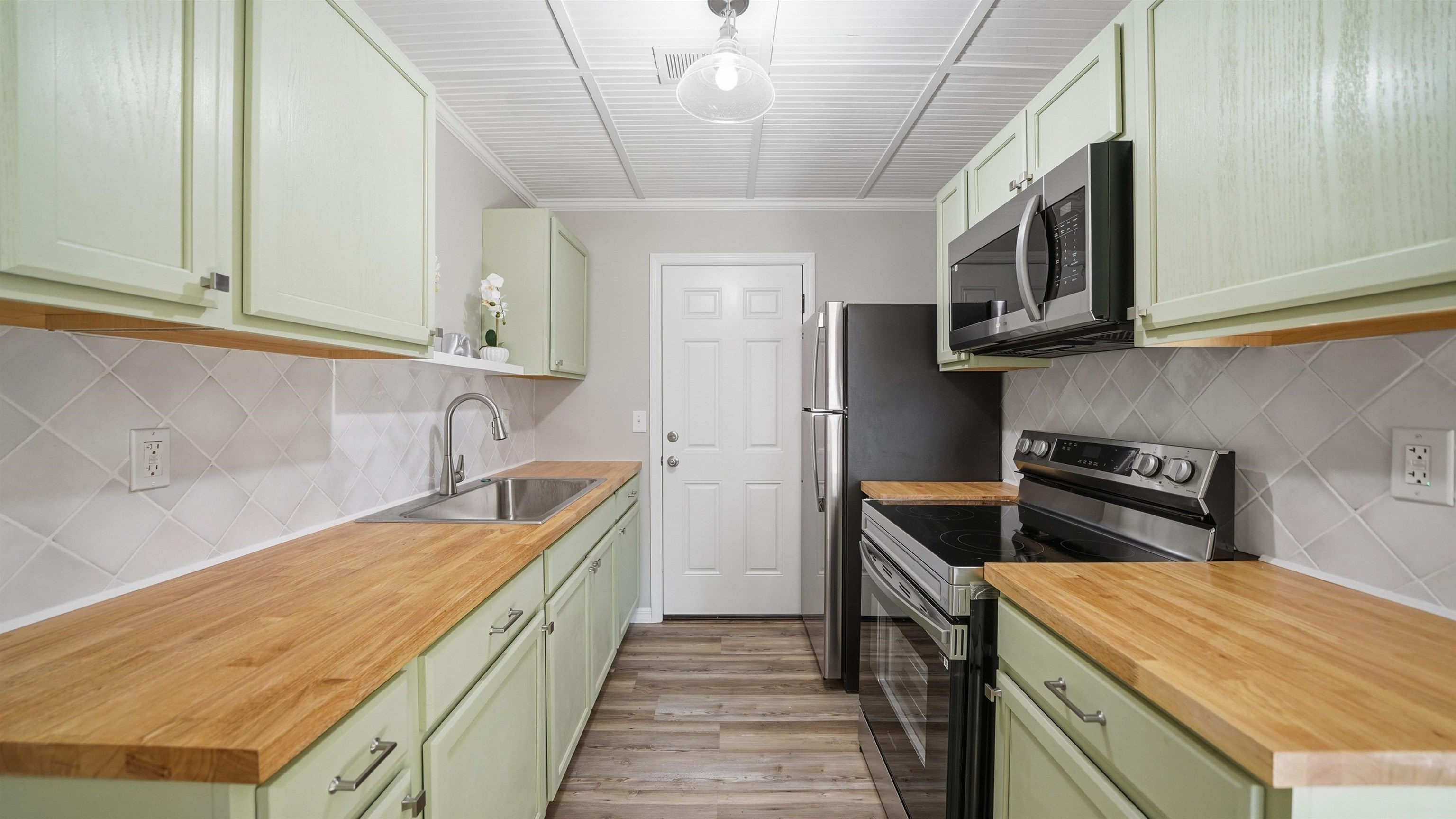 811 Hymon Circle Bunnell, FL 32110 - Photo 24 of 32 Kitchen with green cabinetry, stainless steel appliances, tasteful backsplash, light wood-style flooring, and open shelves