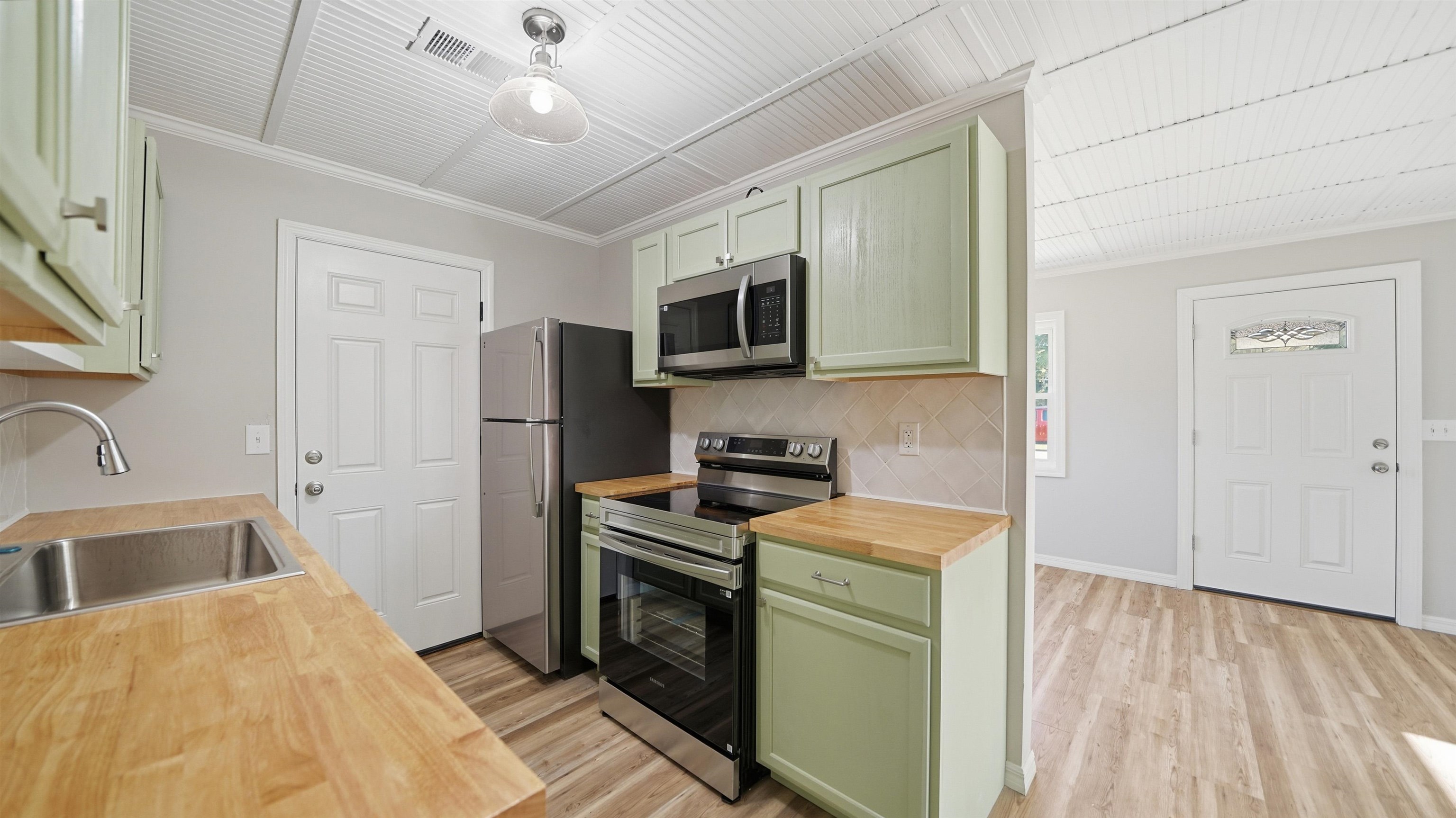 811 Hymon Circle Bunnell, FL 32110 - Photo 25 of 32 Kitchen featuring green cabinetry, butcher block counters, stainless steel appliances, ornamental molding, and light wood-type flooring