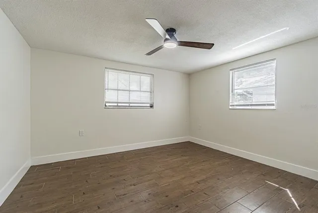 an empty room with wooden floor ceiling fan and window