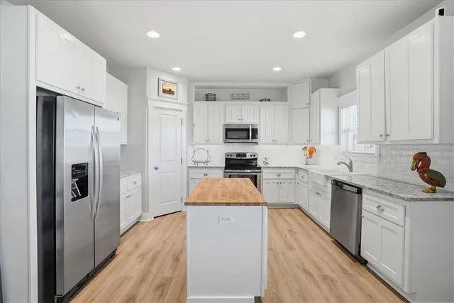 a kitchen with granite countertop a refrigerator a sink dishwasher a stove and white cabinets with wooden floor