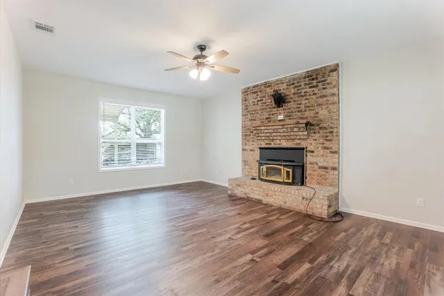 a view of an empty room with wooden floor and a fireplace