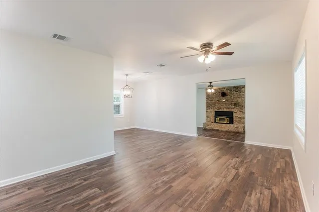 an empty room with wooden floor chandelier fan and windows