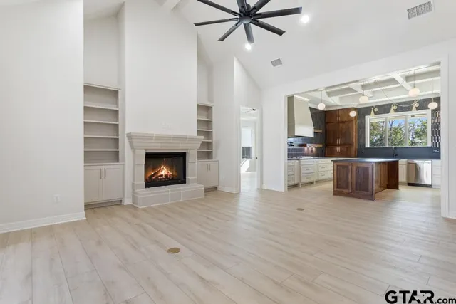 a view of a livingroom with a fireplace a ceiling fan a kitchen wooden floor and a fireplace