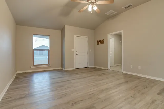 an empty room with wooden floor chandelier fan and windows