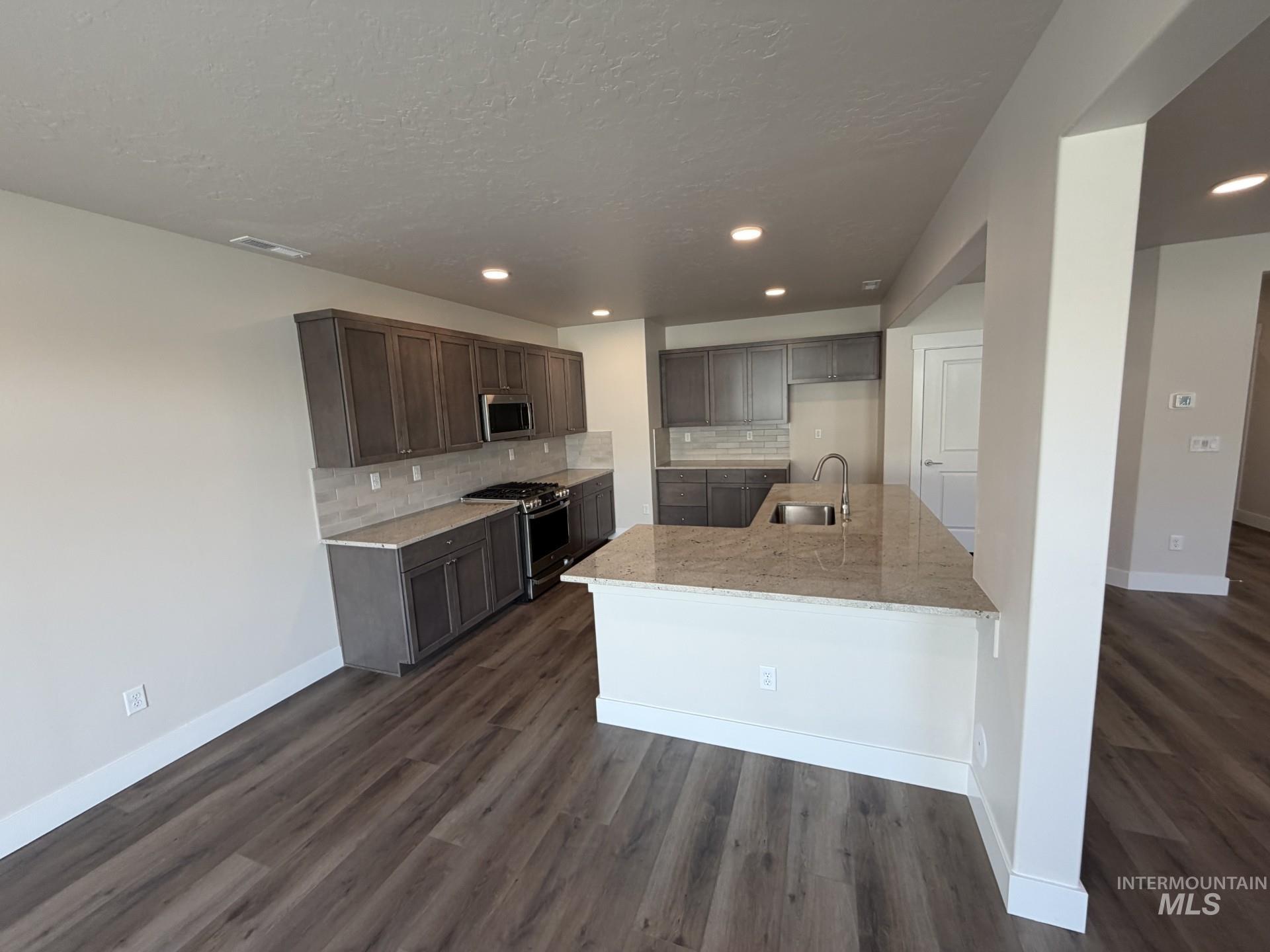 Tbd East Fitz Roy Street, Unit TALENT Kuna, ID 83634 - Photo 2 of 23 Kitchen with decorative backsplash, dark wood finish cabinets, stainless steel appliances, dark wood-style flooring, and light stone countertops