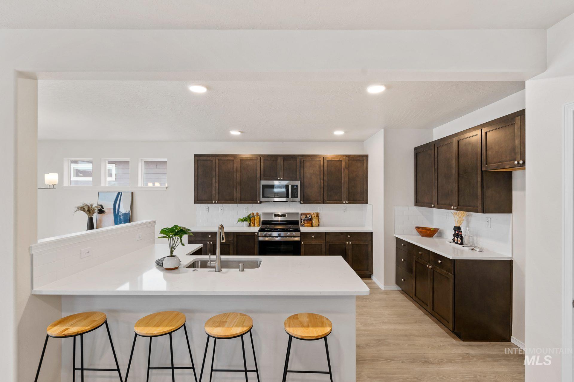 Tbd East Fitz Roy Street, Unit TALENT Kuna, ID 83634 - Photo 4 of 23 Kitchen featuring a kitchen breakfast bar, a peninsula, stainless steel appliances, light wood-style flooring, and dark wood finish cabinets