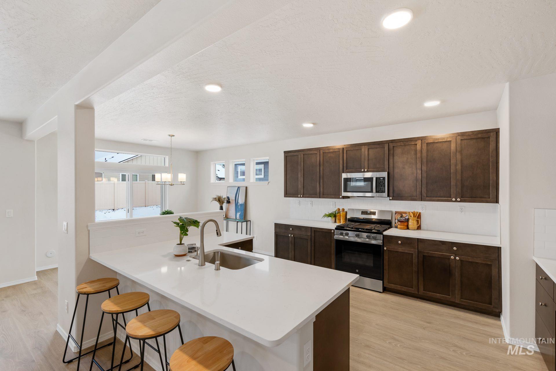 Tbd East Fitz Roy Street, Unit TALENT Kuna, ID 83634 - Photo 5 of 23 Kitchen featuring a kitchen bar, light wood-style floors, stainless steel appliances, dark wood finish cabinets, and a textured ceiling