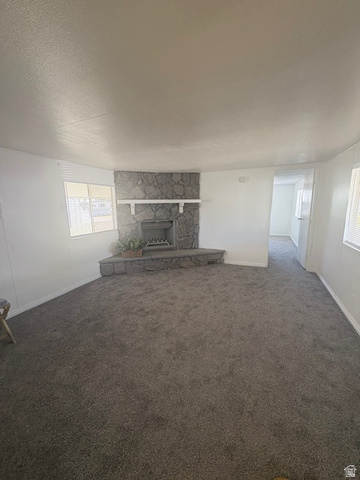 1111 North 2000 West, Unit 293 Farr West, UT 84404 - Photo 3 of 13 Spacious living area featuring a stone-clad fireplace with a hearth and mantel, gray carpet flooring, white painted walls, and multiple windows with blinds
