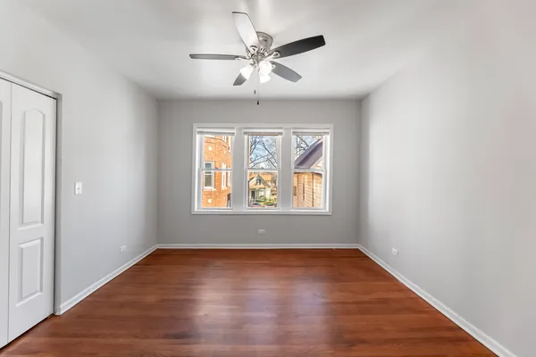 an empty room with wooden floor chandelier fan and windows