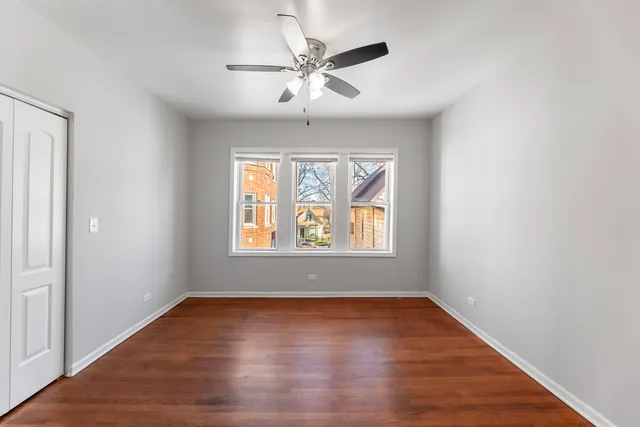 an empty room with wooden floor chandelier fan and windows