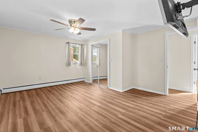 a view of an empty room with wooden floor and a ceiling fan