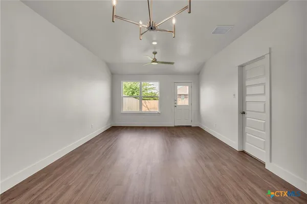 an empty room with wooden floor chandelier fan and windows