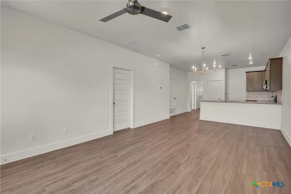 an empty room with wooden floor kitchen view and a refrigerator