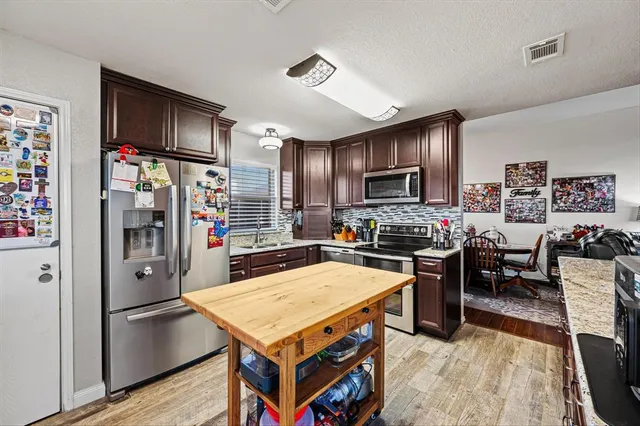 a kitchen with stainless steel appliances granite countertop a refrigerator a stove top oven a sink dishwasher and white cabinets with wooden floor