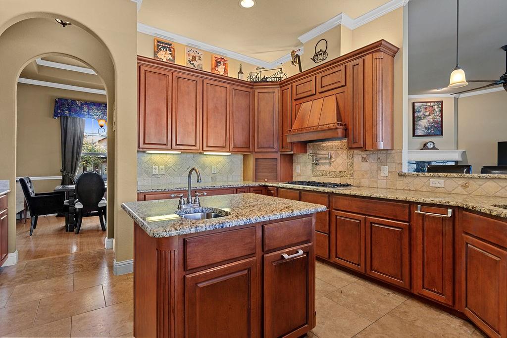 117 Citation Drive Cresson, TX 76035 - Photo 14 of 40 Kitchen featuring pendant lighting, light stone countertops, a center island with sink, backsplash, and ornamental molding