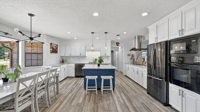 a kitchen with stainless steel appliances a dining table chairs stove refrigerator and cabinets