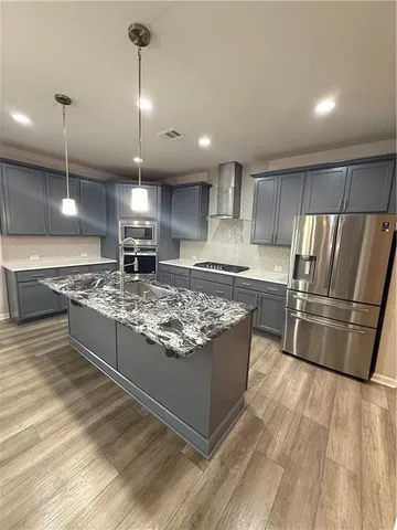 a large kitchen with stainless steel appliances granite countertop a stove a refrigerator a sink a center island and wooden floor