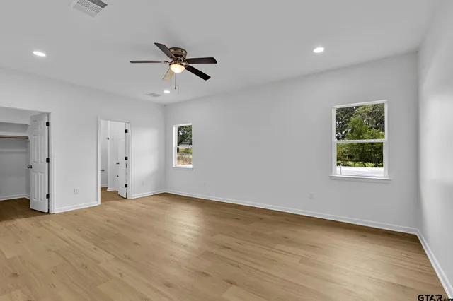 an empty room with wooden floor ceiling fan and windows