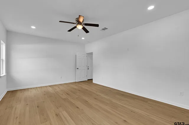 a view of an empty room with wooden floor and a ceiling fan