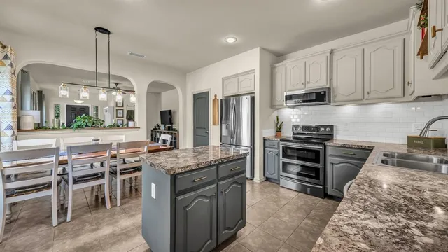 a kitchen with kitchen island granite countertop a stove top oven a sink a dining table and chairs