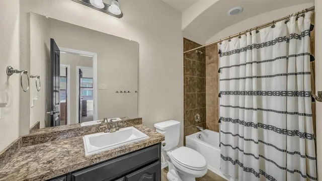 a bathroom with a granite countertop sink toilet a mirror and shower curtain