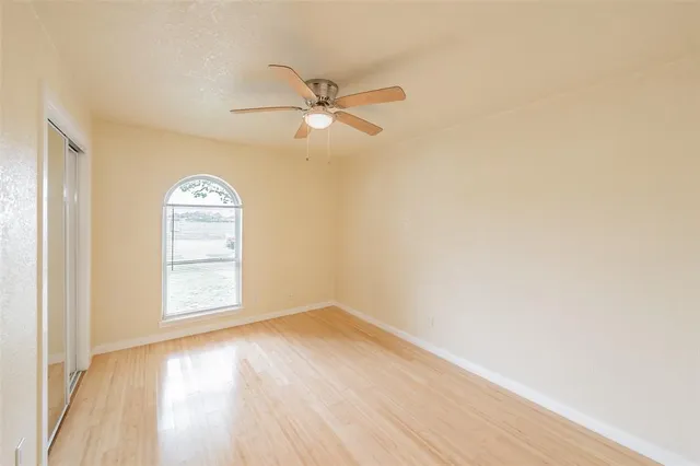 an empty room with wooden floor fan and windows