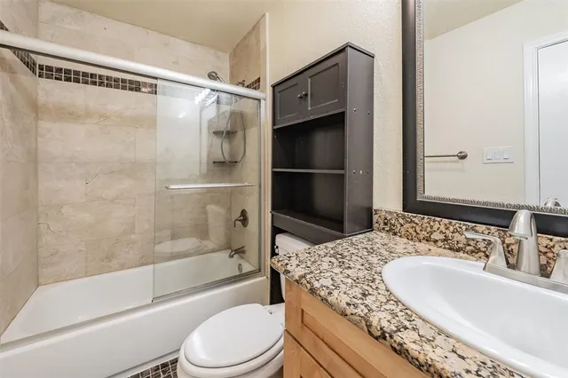 a bathroom with a granite countertop bathtub shower sink vanity and toilet