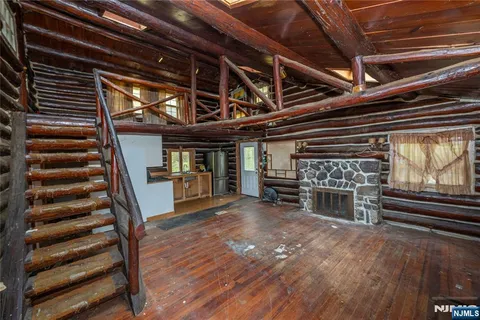 a view of an empty room with stairs wooden floor windows and a fireplace