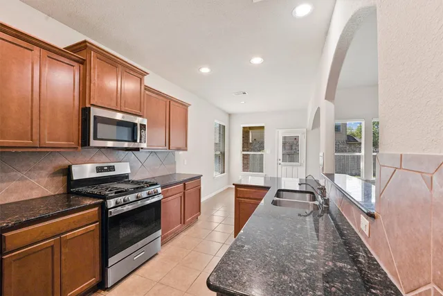 a large kitchen with stainless steel appliances granite countertop a stove top oven a sink dishwasher a dining table and chairs with wooden floor