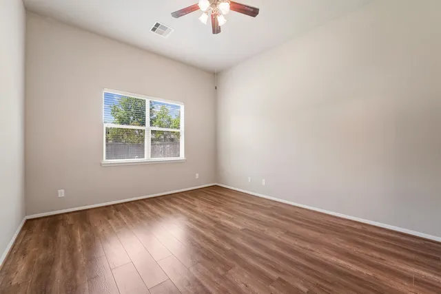 an empty room with wooden floor chandelier fan and windows