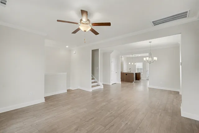 a view of an empty room with wooden floor and a ceiling fan