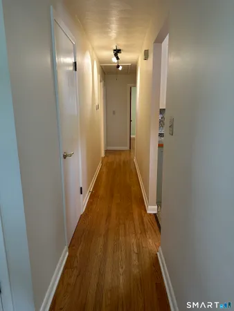 a view of a hallway with wooden floor and a bathroom