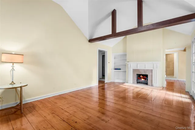 a view of an empty room with wooden floor fireplace and a window