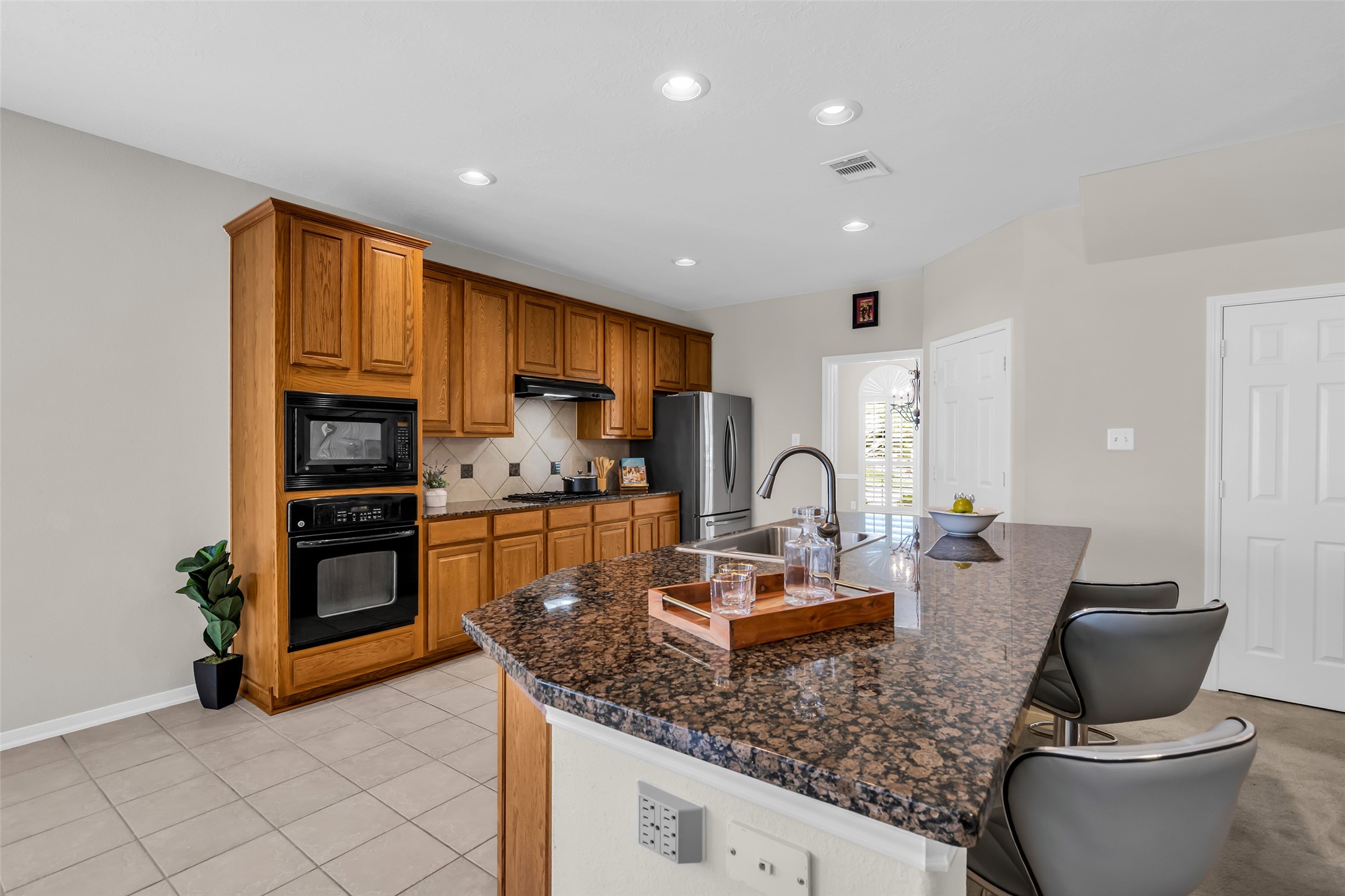 6807 Chapelfield Lane Houston, TX 77049 - Photo 18 of 42 Spacious kitchen with warm wood cabinetry, granite countertops, and a central island with a sink. Features built-in double ovens, tile flooring, and modern lighting.