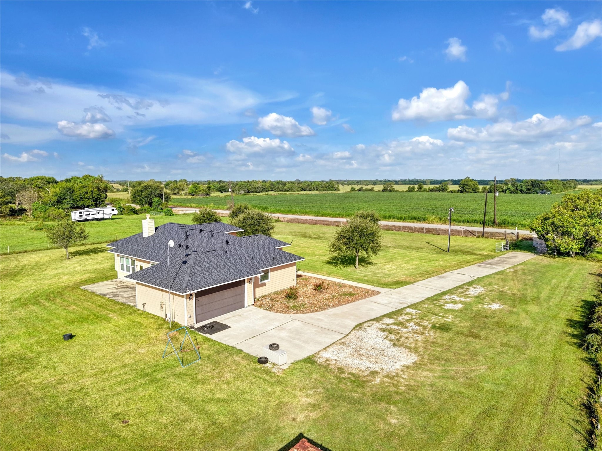 8131 Brinkmeyer Road Needville, TX 77461 - Photo 10 of 49 Charming single-story home with a spacious driveway, nestled amidst expansive green fields and open skies, offering serene country living.